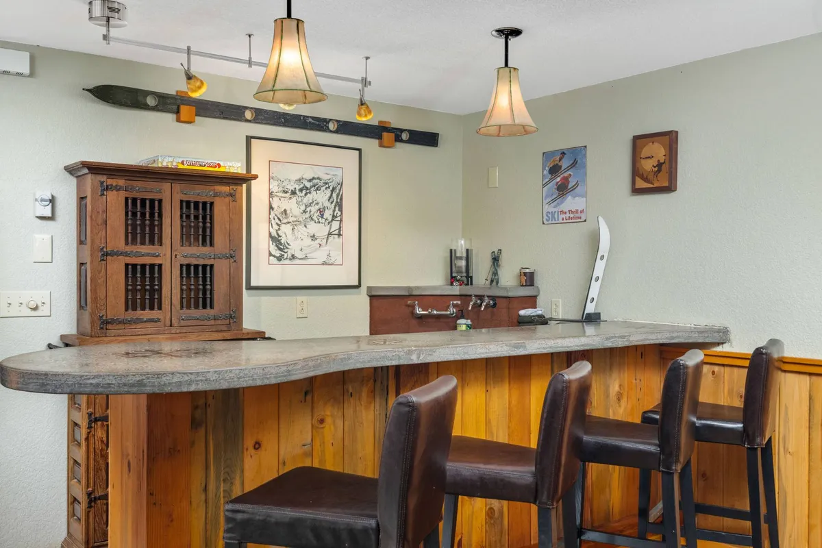 A stylish wet bar with a wooden counter, cabinetry, and warm lighting, set for socializing and entertaining. The setting radiates a cheerful, convivial atmosphere, ideal for après-ski drinks and storytelling.