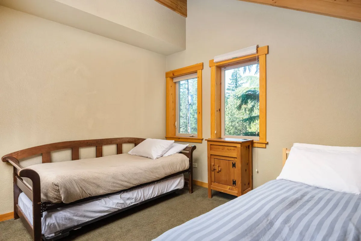 A cozy room with two beds, wooden furniture, and windows that open to views of nature. The welcoming mood invites guests to share bedtime stories or enjoy a restful night's sleep in comfort.