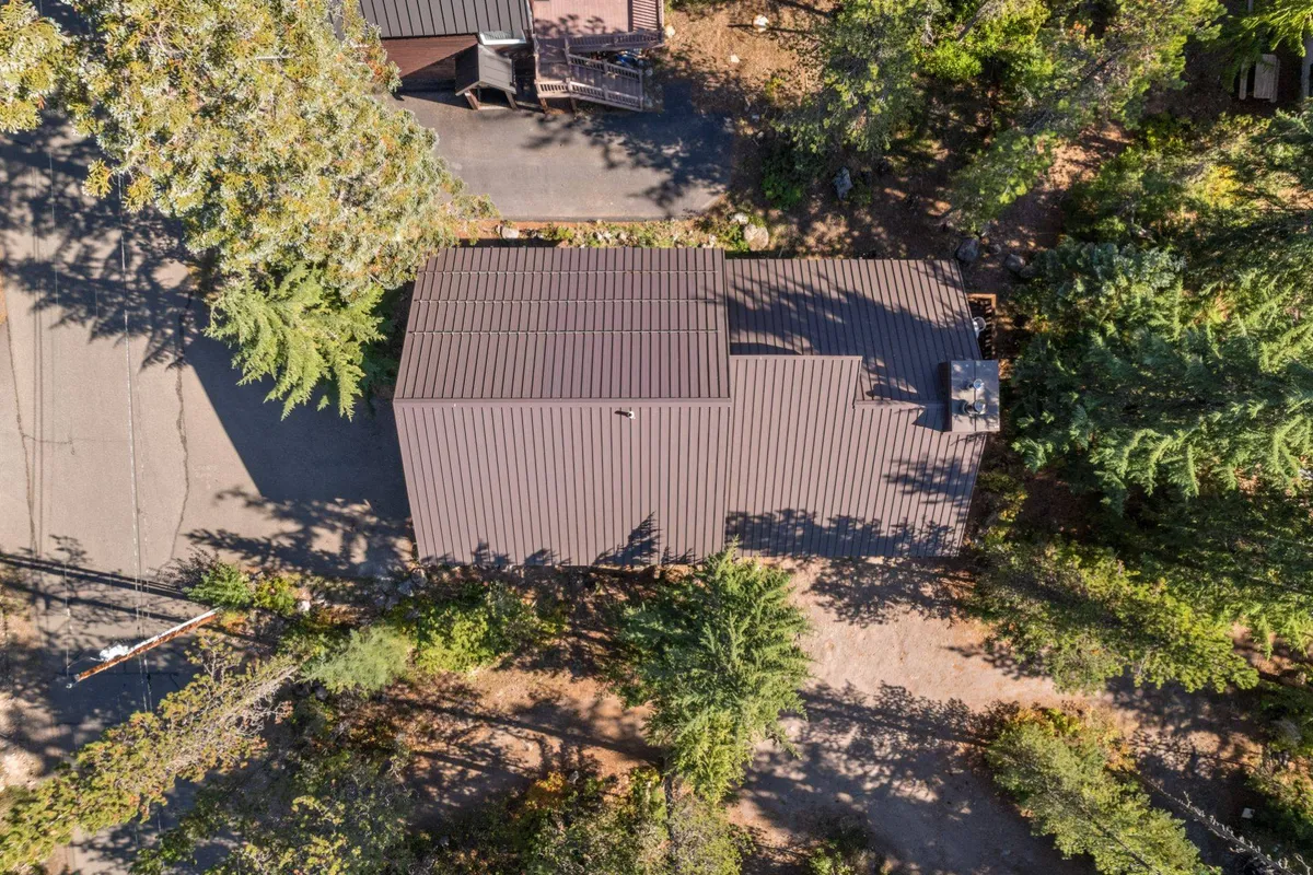 A welcoming exterior view of the home, framed by tall trees and a serene driveway. The roof structure and surrounding natural environment set a peaceful mood and hint at spaces for outdoor gatherings and relaxation.