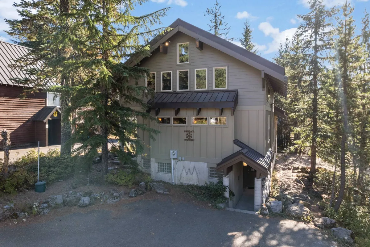 This image captures the exterior of the property, featuring large windows that reveal a welcoming glow from within, a clear view of the front entrance, and a serene backdrop of surrounding trees. The setting evokes a true mountain lodge experience and hints at the proximity to nature and outdoor adventure.