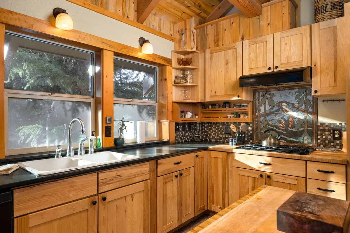 A chef-inspired kitchen space with wooden cabinetry, black countertops, a kitchen island, and an eye-catching decorative tile backsplash. The functional yet cozy space is ready for cooking, baking, and entertaining.