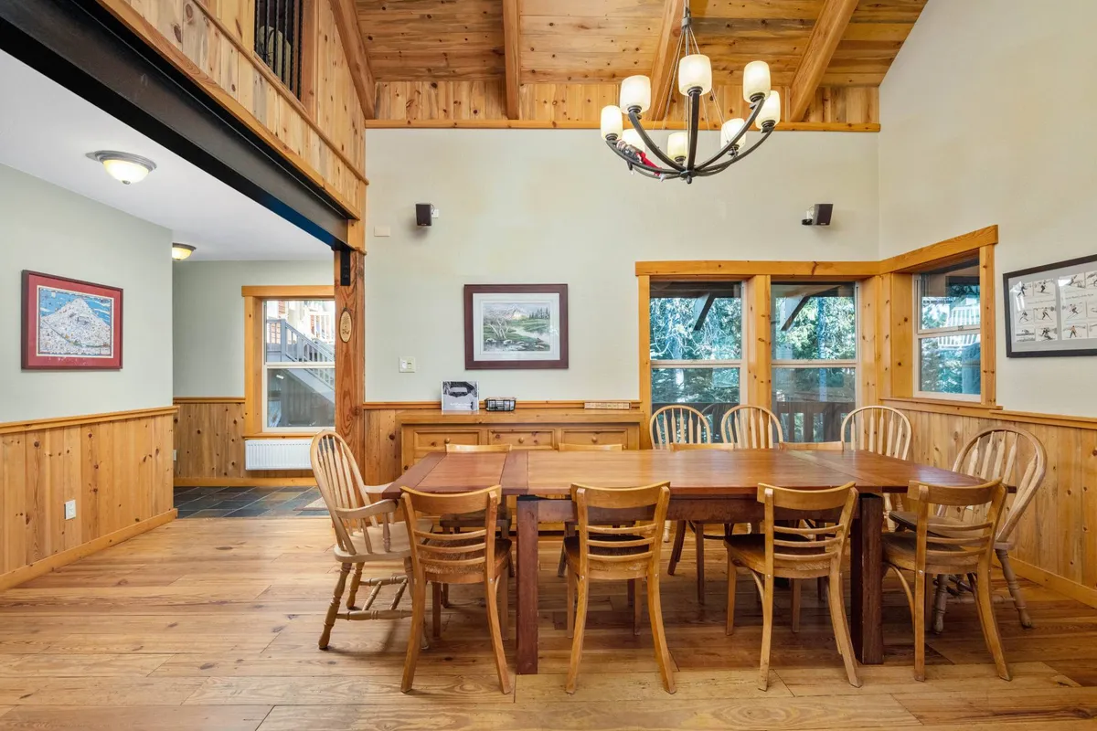 A closer look at a large wooden dining table positioned by windows that offer mountain views, enhanced by a decorative chandelier above. The inviting setting is ready for family dinners, game nights, or celebrations with friends.