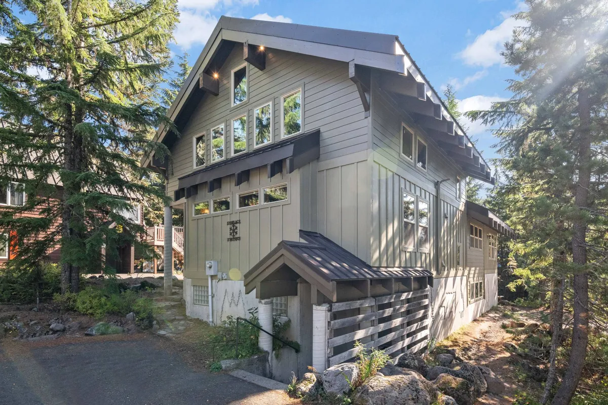 An inviting exterior view with striking large windows, a sloped roof, wood accents, and tall trees surrounding the home. The space feels both secluded and inviting, perfect for gatherings after a day in the snow or for observing the winter landscape from indoors.